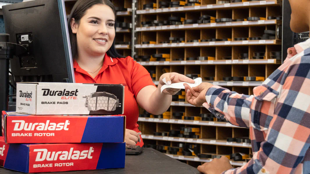 AutoZone employee handing customer a receipt for brake pads and rotors purchase