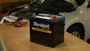 Duralast Gold battery on a shop table in front of an open Nissan Altima.