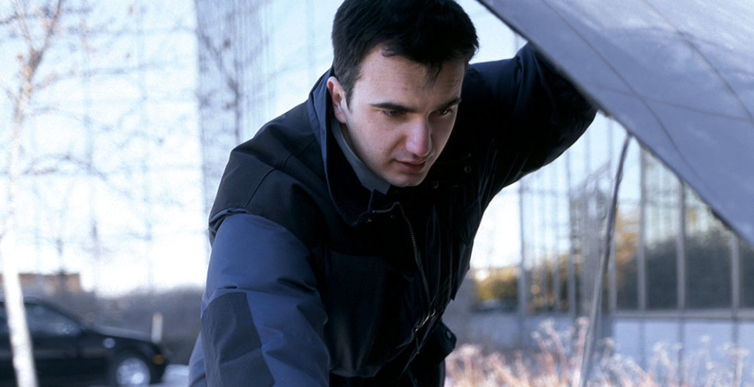 Man looking forlornly under his hood where there is a dead car battery.