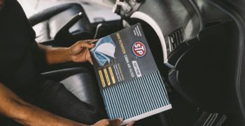 Man removing an STP max filtration cabin air filter from the packaging while sitting in the passenger seat of a car.