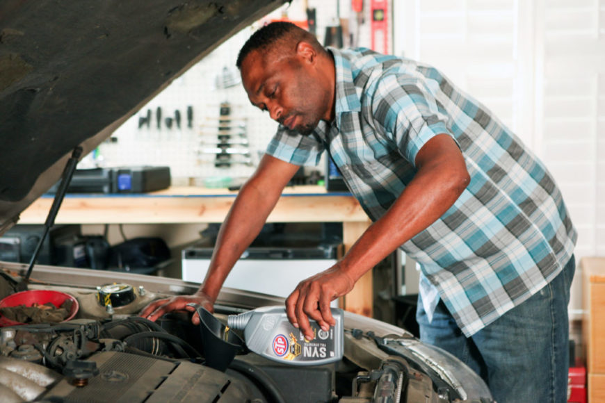 Man pouring STP synthetic oil into his car's engine.