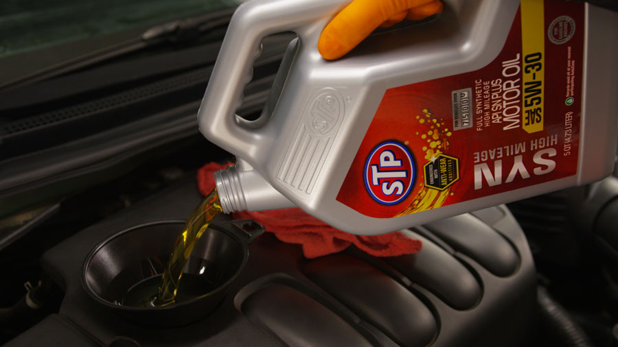 Person pouring STP full synthetic oil into their engine.