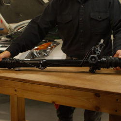 Man holding rack and pinion on a table in the garage with a Nissan Altima in the background.