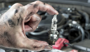 Person holding a damaged spark plug in front of an engine.