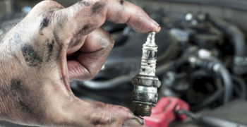 Person holding a damaged spark plug in front of an engine.