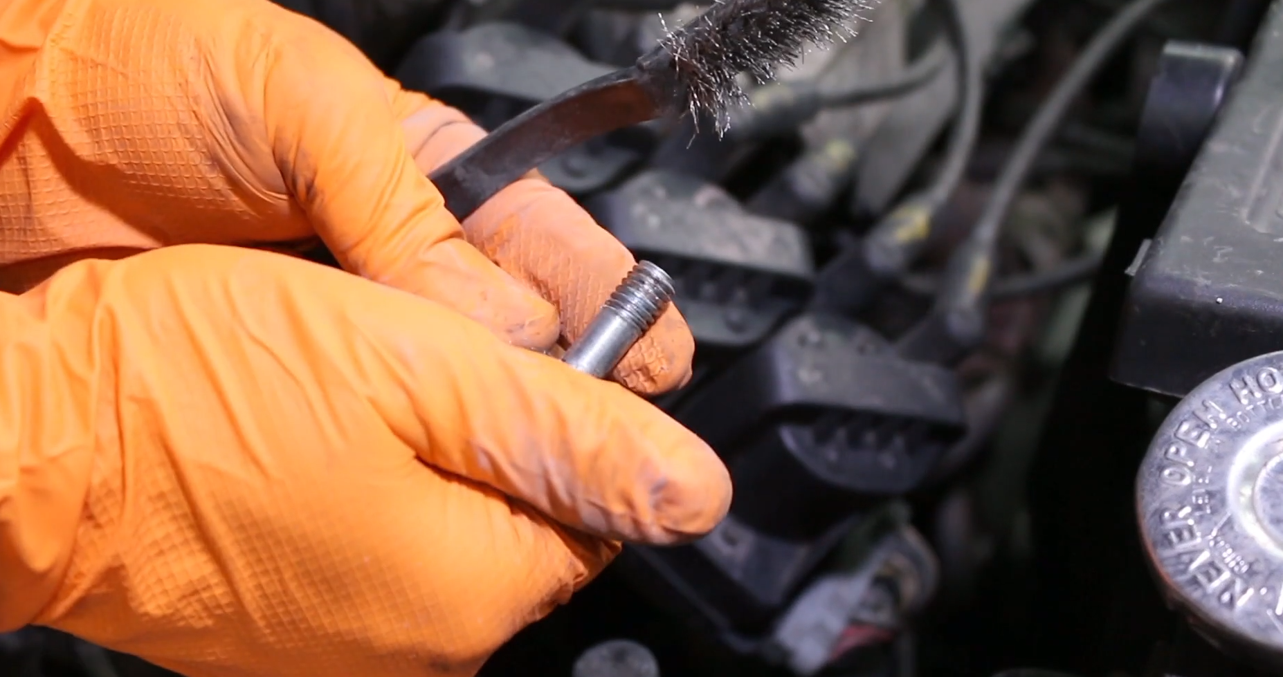 orange gloves holding clean terminal and wire brush used for cleaning