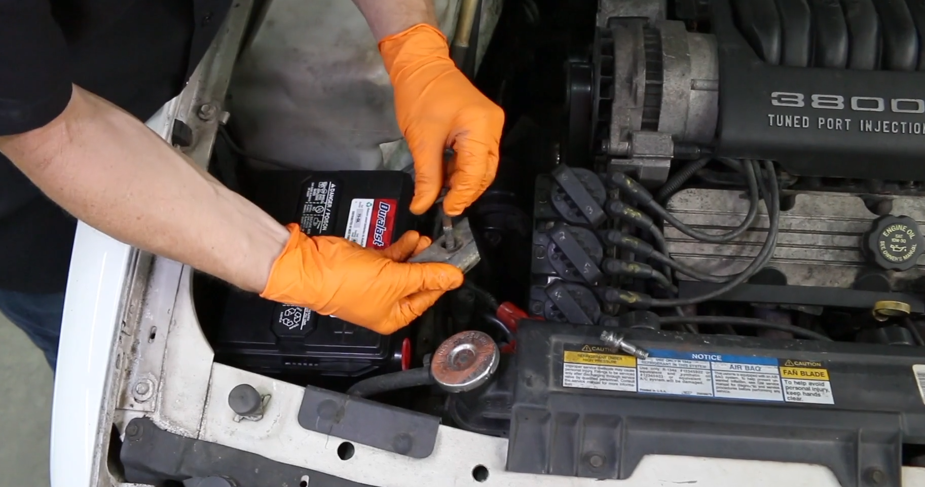 orange gloves showing how to install new battery and clamp to side post battery