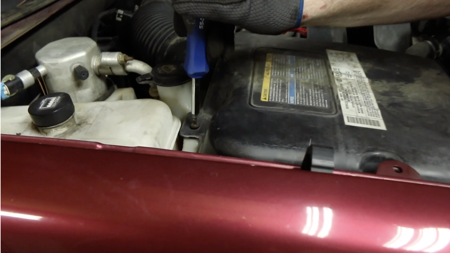 Person using a screwdriver to loosen the air filter cover on a Chevy Trailblazer