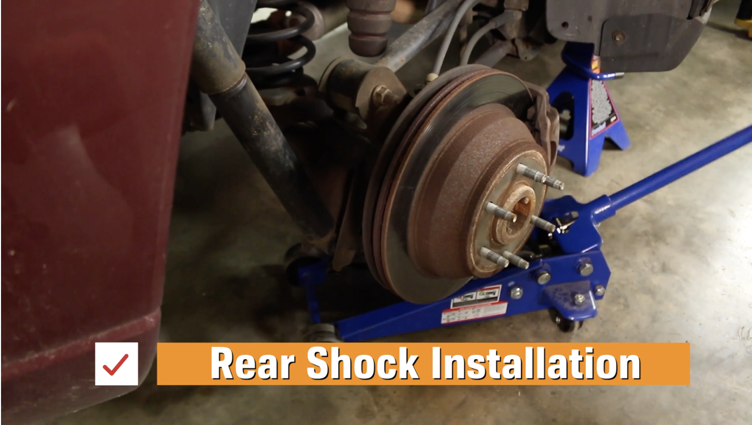 A hydraulic jack placed under a Chevy Trailblazer's lower control arm to install the rear shock