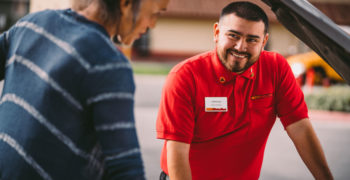 AutoZoner smiling at a customer while both of them stand over a car with an open hood.