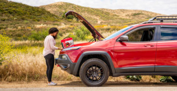 woman standing outside of her car with a roadside emergency kit.