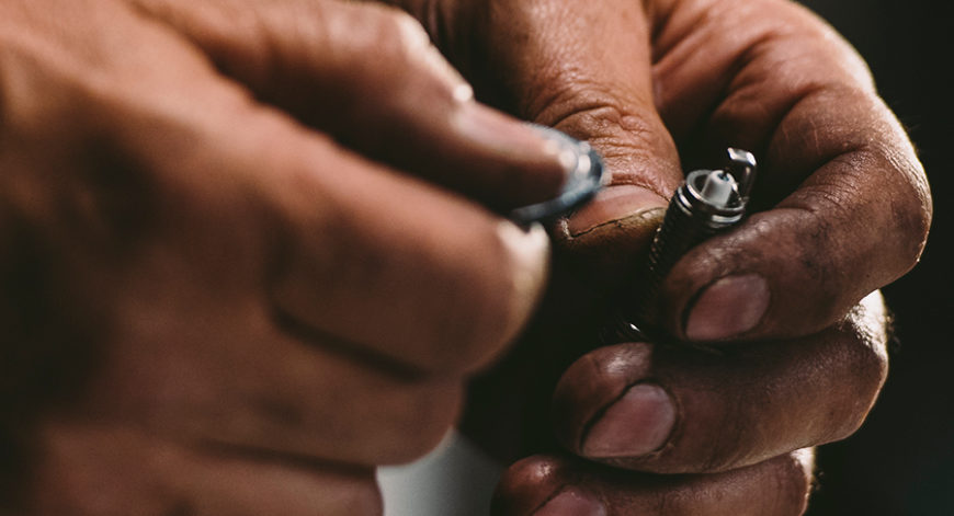 person holding a spark plug in their left hand and a gap tool in the right, preparing to gap a spark plug