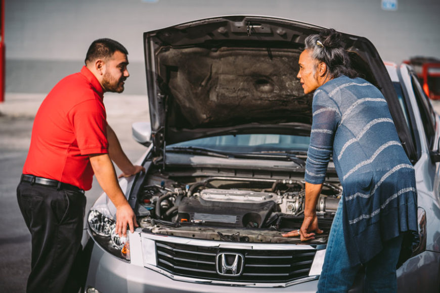 AutoZone associate demonstrating the basic parts of a car under the hood to a customer