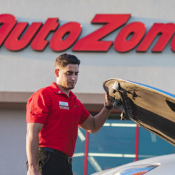 AutoZoner looking inside of the open hood of a car parked out front of the store