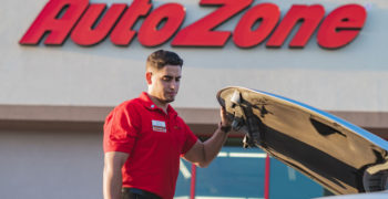 AutoZoner looking inside of the open hood of a car parked out front of the store