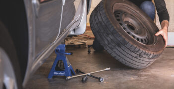 male removing tire from car on duralast jackstand with 4way wrench