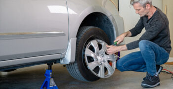 male taking off hub cap on silver car on duralast jackstand