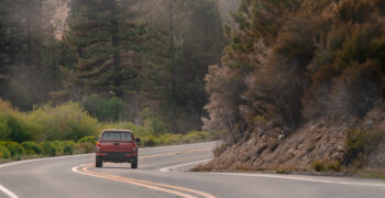 red truck driving down wooded highway 2